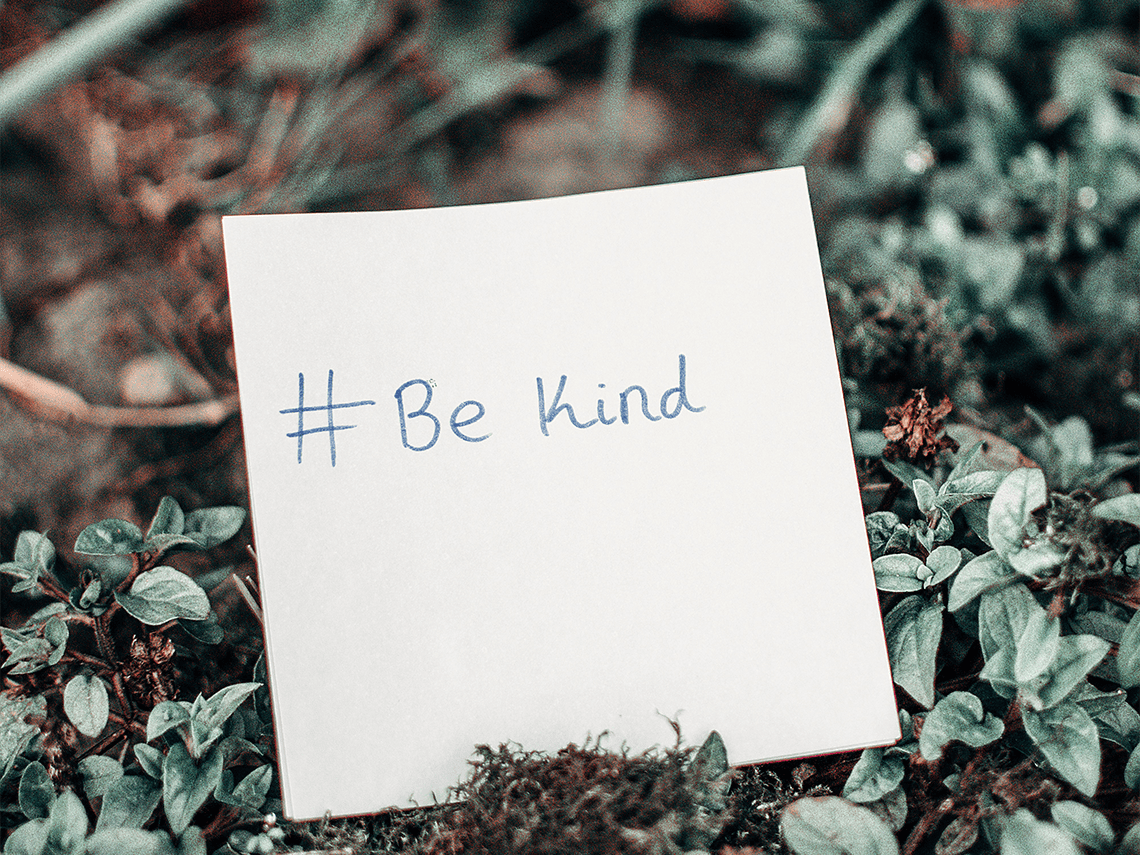 un morceau de papier posé sur des feuilles au sol avec "#be kind" écrit en lettres bleues
